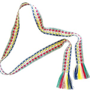 Puede incluir: Un cintur&oacute;n o faja tejida larga y estrecha con un patr&oacute;n geom&eacute;trico repetitivo en hilos rojos, amarillos, azules y blancos. Los extremos del cintur&oacute;n est&aacute;n terminados con borlas de flecos multicolores en tonos verde, rojo, amarillo, blanco y azul.
