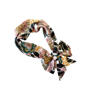 May include: A fabric headband featuring a vibrant, multi-colored floral and geometric pattern in shades of mustard yellow, deep green, black, and soft pink. The accessory is tied into a decorative bow knot on one side, creating a structured loop.