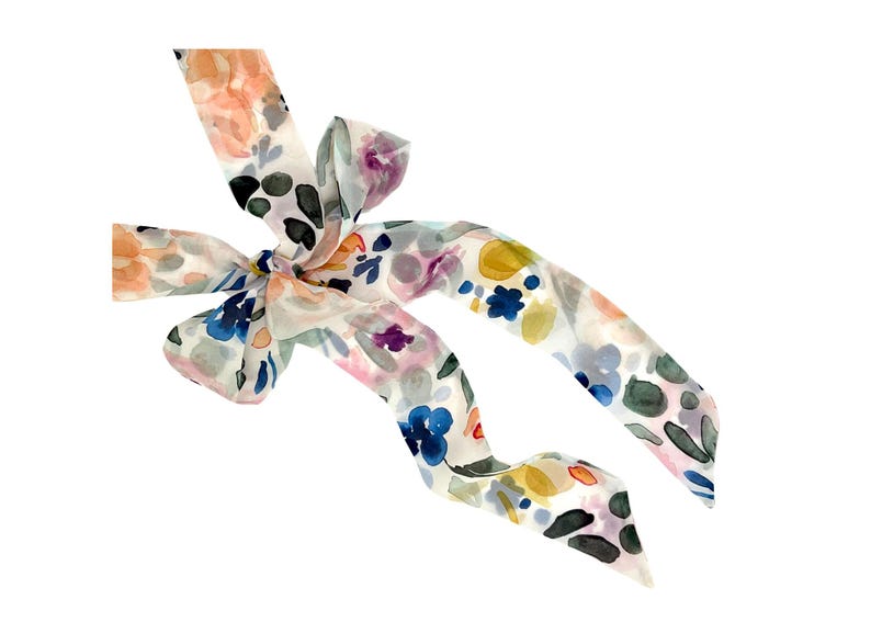 May include: A floral patterned scarf with a bow. The scarf features watercolor-style flowers in shades of orange, blue, purple, and green on a white background. The scarf is tied in a bow.