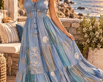 May include: A floor-length blue maxi dress featuring a V-neckline, thin spaghetti straps, and a cinched elastic waist with tassel ties. The fabric is adorned with a gold metallic print of seashells, starfish, and coral patterns throughout.