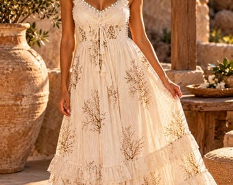 May include: A floor-length cream-colored dress featuring a brown tree-branch pattern, thin spaghetti straps, a ruffled neckline with small blue accents, a drawstring waist with tassels, and a tiered skirt with ruffled hem details throughout.