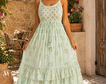 May include: A floor-length, light mint green sleeveless dress featuring a scoop neckline, thin shoulder straps, and a drawstring waist with tassels. The fabric is adorned with a metallic gold circular pattern and two tiered ruffled hem layers.