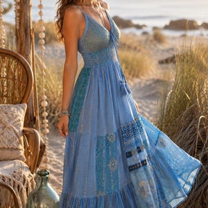 May include: A floor-length blue maxi dress featuring a V-neckline, thin spaghetti straps, and a smocked waist. The garment is constructed from multiple panels of blue fabric with varying patterns and gold metallic accents, including tassels.