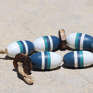 May include: A string of blue, white, and green striped wooden beads with a brown wooden bead at the end. The beads are connected with a natural twine string.