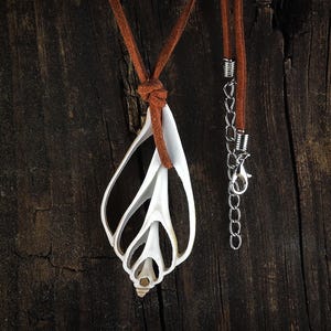 May include: A white seashell pendant necklace with a brown leather cord. The necklace is hanging on a dark brown wooden surface.
