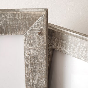 May include: Two rustic wooden picture frames with a whitewashed finish. The frames are stacked on top of each other, with the top frame slightly offset to the right. The frames are made of thick, rough-hewn wood with a natural grain pattern. The whitewash paint gives the frames a distressed, vintage look.
