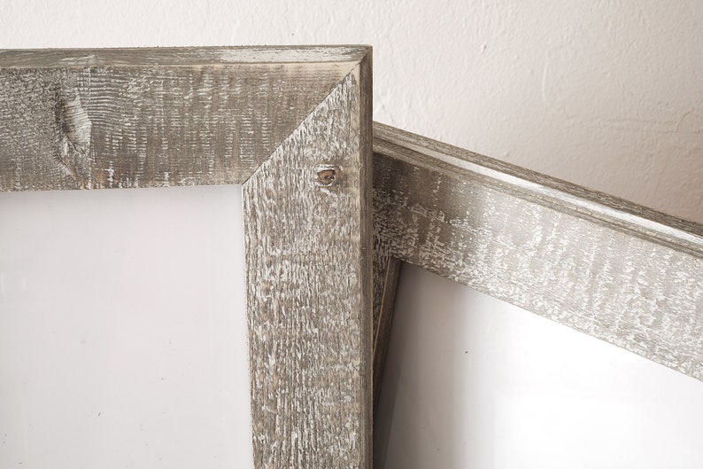May include: Two rustic wooden picture frames with a whitewashed finish. The frames are stacked on top of each other, with the top frame slightly offset to the right. The frames are made of thick, rough-hewn wood with a natural grain pattern. The whitewash paint gives the frames a distressed, vintage look.