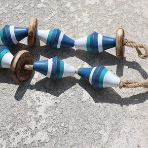 May include: A string of wooden beads with blue, white, and green stripes. The beads are connected with a natural twine rope.