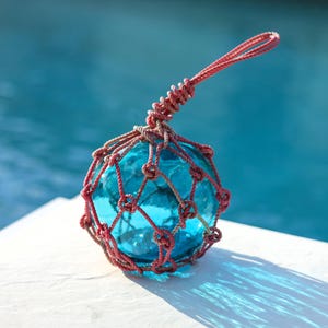 May include: A blue glass float encased in a red rope net. The float is a traditional nautical decoration.