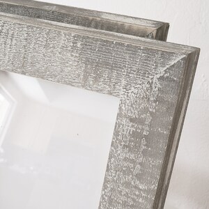 May include: A double picture frame made of wood with a distressed gray finish. The frame has a simple design with a rectangular opening.