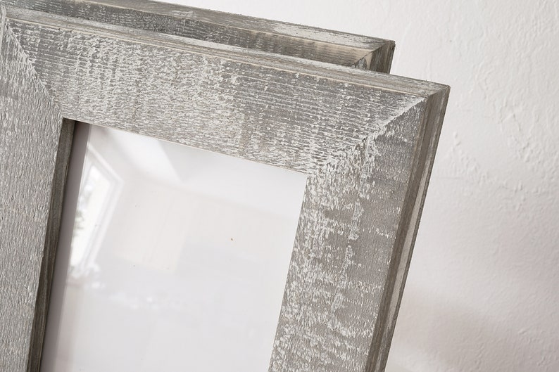 May include: A double picture frame made of wood with a distressed gray finish. The frame has a simple design with a rectangular opening.