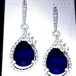 May include: A pair of silver-toned drop earrings. Each earring features a large, teardrop-shaped, deep blue stone surrounded by smaller, clear stones. The top portion of each earring has a slender, elongated design with more clear stones.