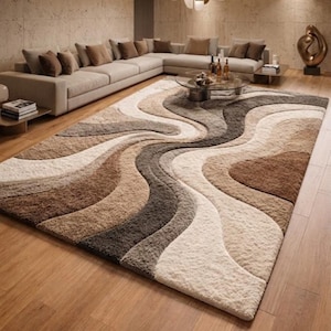 Op de afbeelding: Een groot, zacht vloerkleed met een vloeiend, abstract ontwerp in tinten bruin, beige en grijs. Het kleed ligt op een houten vloer in een woonkamer en vormt een aanvulling op de neutrale kleurstelling van de ruimte.