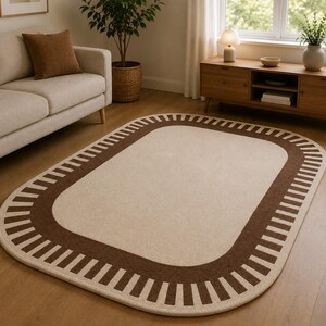 May include: An oval area rug featuring a large cream-colored center surrounded by a wide, dark brown border. The border is decorated with a repeating pattern of short, vertical, cream-colored stripes that extend outward toward the rug's edge.