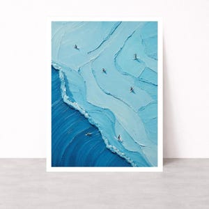 May include: A textured oil painting on canvas depicting an aerial view of a blue ocean with visible brushstrokes. The artwork features several small figures on surfboards and paddleboards scattered across light blue water near a dark blue wave.