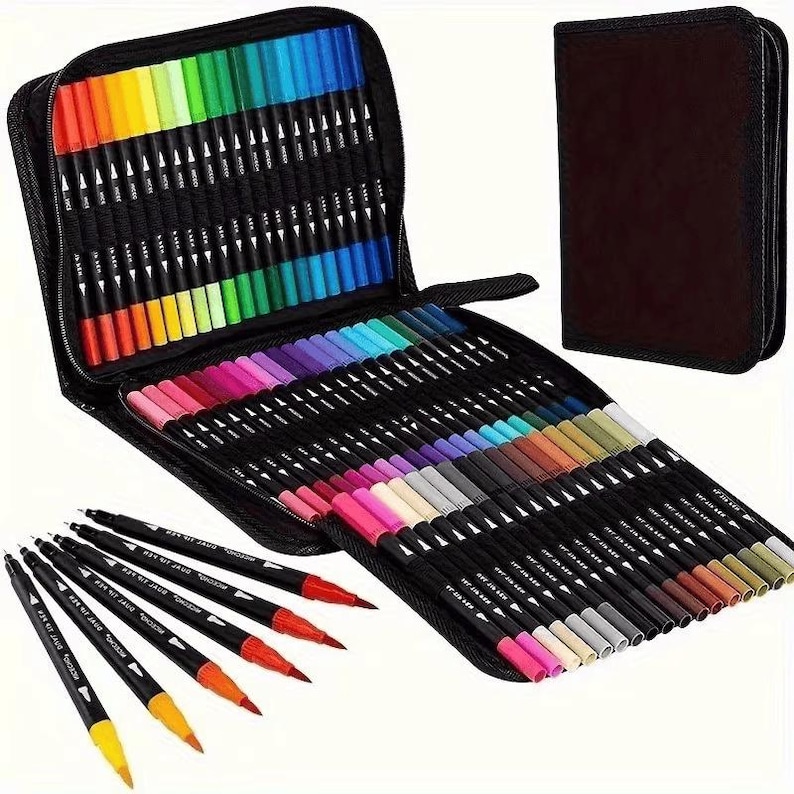 May include: A black zipped case containing a vibrant array of dual-tip markers, arranged in colour order. A closed brown case is also present. Several individual markers are visible, showcasing their dual tips and colour variations.