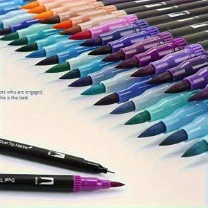 May include: A selection of dual-tip markers in various colours, arranged at an angle. Each marker has a black barrel with a fine tip and a brush tip. The colours include orange, pink, red, purple, blue, and green.
