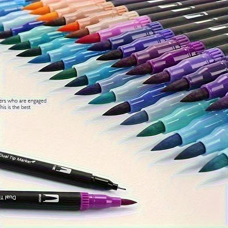 May include: A selection of dual-tip markers in various colours, arranged at an angle. Each marker has a black barrel with a fine tip and a brush tip. The colours include orange, pink, red, purple, blue, and green.