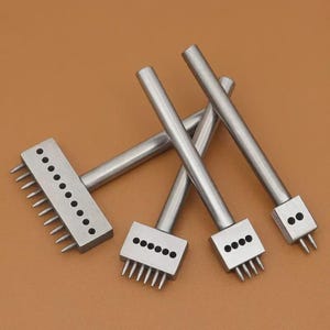 May include: A collection of stainless steel leather working tools. The tools have rectangular heads with evenly spaced tines and circular holes. The handles are cylindrical. The tools are arranged on a brown surface.