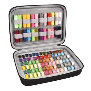 May include: Open black zippered sewing kit filled with colorful thread spools and bobbins. The top section holds thread spools in various colors, secured by gray elastic bands. The bottom section contains a wide array of thread bobbins.
