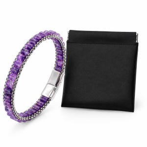 Puede incluir: Una pulsera de amatista púrpura con cierre y cadena plateados. La pulsera está junto a una bolsa negra. La pulsera está hecha de pequeñas piedras de amatista rectangulares. El cierre es plateado y rectangular.