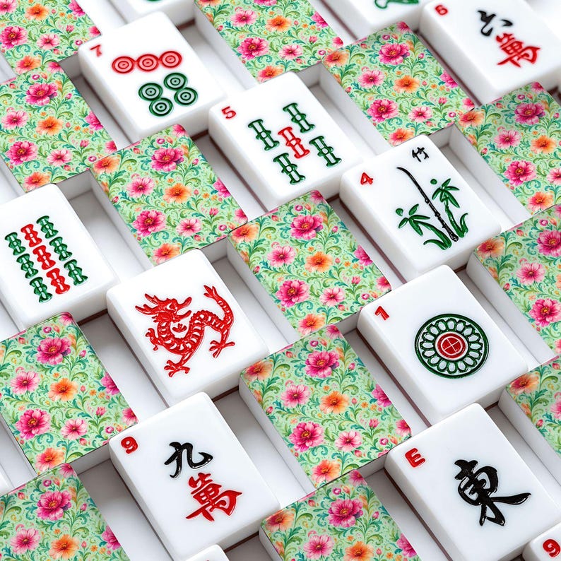 K&ouml;nnte beinhalten: Eine Sammlung von Mahjong-Spielsteinen mit wei&szlig;en Vorderseiten, die rote, gr&uuml;ne und schwarze Symbole, Zahlen und Schriftzeichen zeigen. Zwischen den Spielsteinen befinden sich dekorative R&uuml;ckseiten mit einem lebendigen Blumenmuster aus rosa und orangefarbenen Bl&uuml;ten auf gr&uuml;nem Grund.