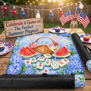 May include: A summer-themed playmat with a picnic basket, watermelon slices, and mahjong tiles. The mat features blue hydrangea flowers and a fireworks design. The sign reads "Celebrate & Game on! - The Perfect Summer Playmat."