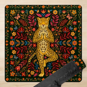 Puede incluir: Una esterilla de yoga con un leopardo dorado en postura de &aacute;rbol, rodeado de un dise&ntilde;o floral con mariposas. La esterilla tiene un fondo verde oscuro con flores rojas, naranjas y amarillas. Se incluye una funda de transporte negra.
