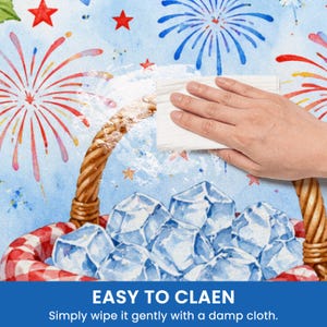 May include: A hand wipes a surface with a white cloth. The surface has a watercolor design of fireworks, stars, and a picnic basket filled with ice. Text at the bottom reads "EASY TO CLEAN" and "Simply wipe it gently with a damp cloth."