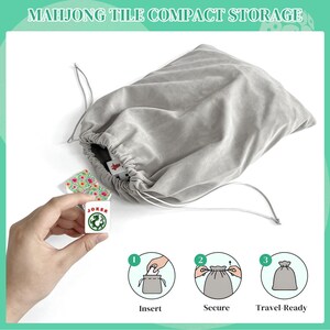 K&ouml;nnte beinhalten: Ein hellgrauer Samtbeutel mit Kordelzug zur kompakten Aufbewahrung von Mahjong-Steinen. Die Tasche hat eine weiche Stoffoberfl&auml;che mit passenden grauen Kordeln. Ein wei&szlig;er Mahjong-Stein mit gr&uuml;nem Drachenmotiv und rotem JOKER-Text.