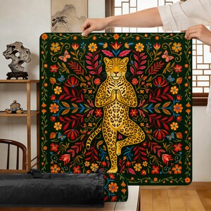 Puede incluir: Una esterilla de yoga cuadrada, verde oscuro, con un leopardo dorado en postura de &aacute;rbol, rodeado de coloridas flores y follaje. El leopardo est&aacute; en una pose meditativa. La esterilla tiene un borde floral.