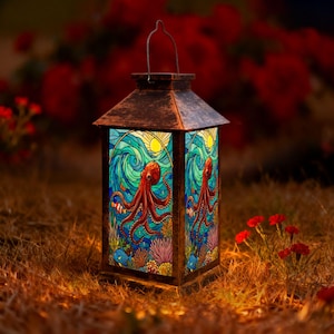 May include: A rectangular lantern with a dark, weathered metal frame and a top handle. The glass panels feature a colourful stained-glass style illustration of a red octopus swimming in blue water with coral, small fish, and a yellow sun.