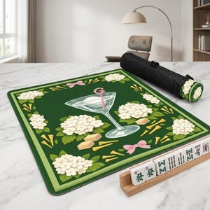 Peut inclure: Tapis de Mahjong vert avec un motif sur le th&egrave;me du golf. Le tapis pr&eacute;sente un verre &agrave; martini avec une balle de golf, des fleurs blanches, des n&oelig;uds roses et des tees de golf. Un &eacute;tui de transport noir et des tuiles de Mahjong sont &eacute;galement visibles.