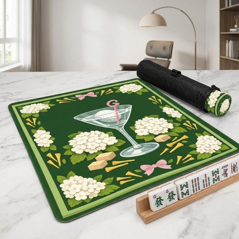 Peut inclure: Tapis de Mahjong vert avec un motif sur le th&egrave;me du golf. Le tapis pr&eacute;sente un verre &agrave; martini avec une balle de golf, des fleurs blanches, des n&oelig;uds roses et des tees de golf. Un &eacute;tui de transport noir et des tuiles de Mahjong sont &eacute;galement visibles.