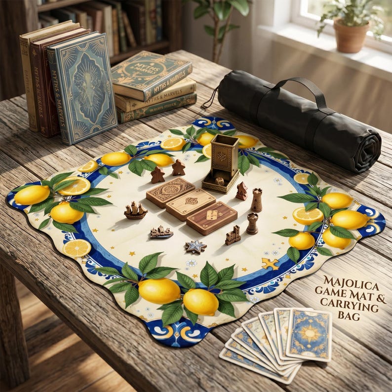 K&ouml;nnte beinhalten: Eine Majolica-Spielmatte mit Zitronen- und Bl&auml;ttermuster, umgeben von Spielsteinen, Karten und einer Tragetasche. Die Matte liegt auf einem Holztisch neben B&uuml;chern mit dem Titel "Myths & Marvels".