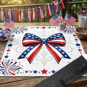 May include: A white placemat with a patriotic bow design in red, white, and blue, surrounded by stars and fireworks. The scene includes American flags, decorative items, and a wooden table, perfect for a festive celebration.