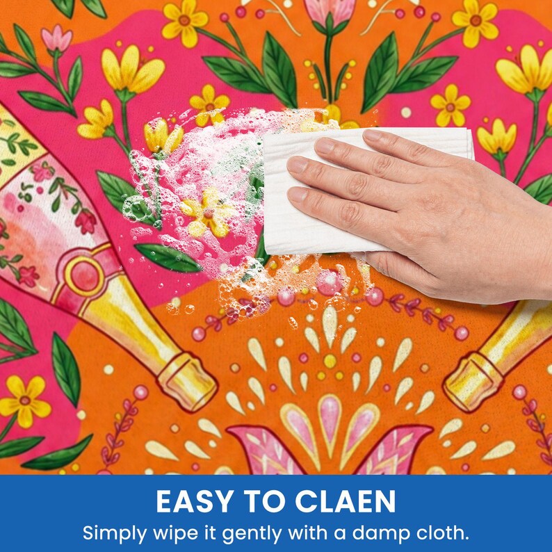 May include: A hand wipes a colorful floral patterned surface with a white cloth, creating suds. The design features champagne bottles and flowers in pink, orange, and yellow. Text at the bottom reads "EASY TO CLEAN".
