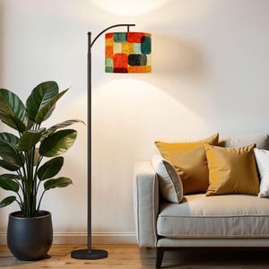 May include: A tall, slender floor lamp with a dark metal base and a curved arm. The cylindrical lampshade features a vibrant, multi-coloured pattern of overlapping rounded rectangles in shades of red, orange, yellow, teal, and black.