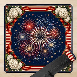 May include: A square rug with a patriotic theme. The rug features a dark blue background with a fireworks display in red, white, and blue. White flowers and red ribbons adorn the corners. A black carrying case is visible in the lower right corner.