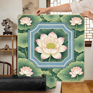 May include: A square, floral-themed mat featuring a central lotus flower with pink and white petals, surrounded by green leaves. The design includes a light blue frame and four additional lotus flowers. The mat is held up by a person.