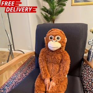 May include: A plush orangutan stuffed animal with shaggy, rust-colored fur, a light beige face, and large, dark eyes. The toy is seated upright, featuring a soft, textured body and a gentle expression, designed with realistic facial features.