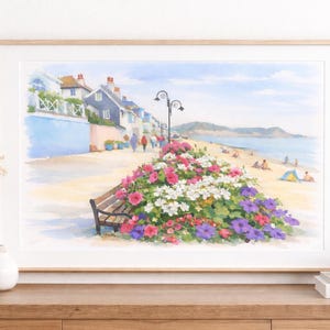 May include: A framed watercolor painting depicts a seaside scene with a bench, flowers, and people on a beach. The artwork features a bench surrounded by pink, white, and purple flowers. Buildings line the shore under a blue sky.