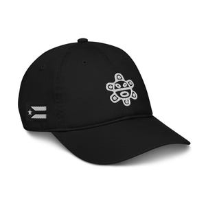 Puede incluir: Gorra de béisbol negra con un diseño bordado blanco en la parte delantera y una bandera de Puerto Rico en el lateral. La gorra tiene una visera curva y una corona redondeada. El diseño bordado es un símbolo solar estilizado.