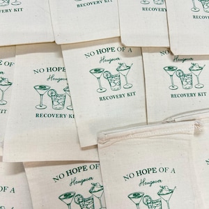 May include: A collection of off-white canvas bags with green text and illustrations. Each bag features the phrase "NO HOPE OF A Hangover" above a drawing of cocktails and the words "RECOVERY KIT" below. The bags are arranged in a slightly overlapping pattern.