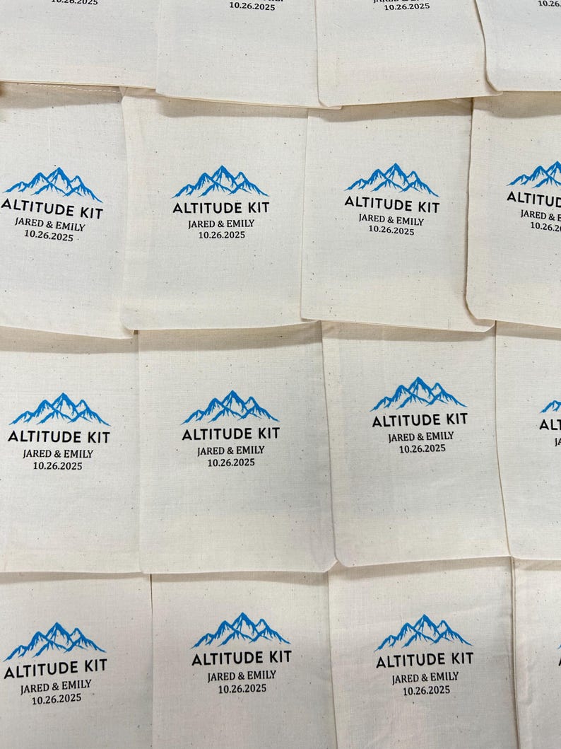 May include: Off-white fabric pouches with a blue mountain graphic and the text "ALTITUDE KIT JARED & EMILY 10.26.2025". The pouches are arranged in a grid pattern. The design is simple and clean.