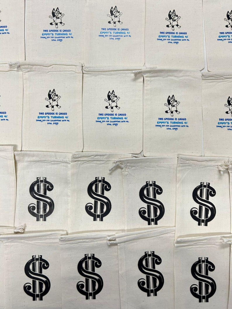 May include: Off-white canvas bags with black printed dollar signs and text. Some bags feature a cartoon character and the text "THIS EPISODE IS CALLED EMMY'S TURNING 4!" in blue. The bags are likely for party favors.