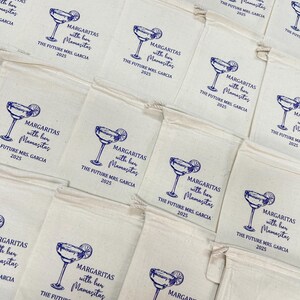 May include: Off-white drawstring bags with a blue margarita glass design and text that reads "MARGARITAS with her Mamasitas THE FUTURE MRS. GARCIA 2025". The bags are arranged in a grid pattern.