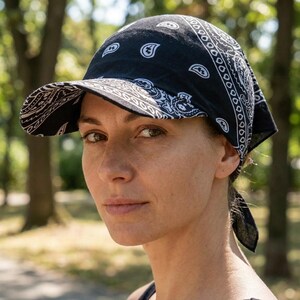 May include: A black bandana-style cap featuring a white paisley print pattern. The headwear includes a stiffened brim and fabric ties at the back, constructed from a lightweight material with a classic repeating teardrop and floral motif design.