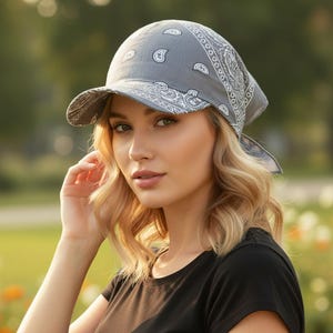 May include: A grey bandana-style cap featuring a white paisley print pattern. The headwear has a structured brim and fabric ties at the back, constructed from a lightweight material with a classic repeating teardrop and floral motif design.
