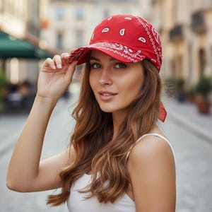 May include: A bright red baseball cap featuring a white paisley bandana print pattern. The cap has a structured crown and a curved brim, with fabric ties extending from the back, creating a distinct headwear piece with a classic bandana aesthetic.